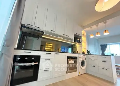 Modern kitchen with sleek white cabinets, built-in oven, and washing machine in open layout design.