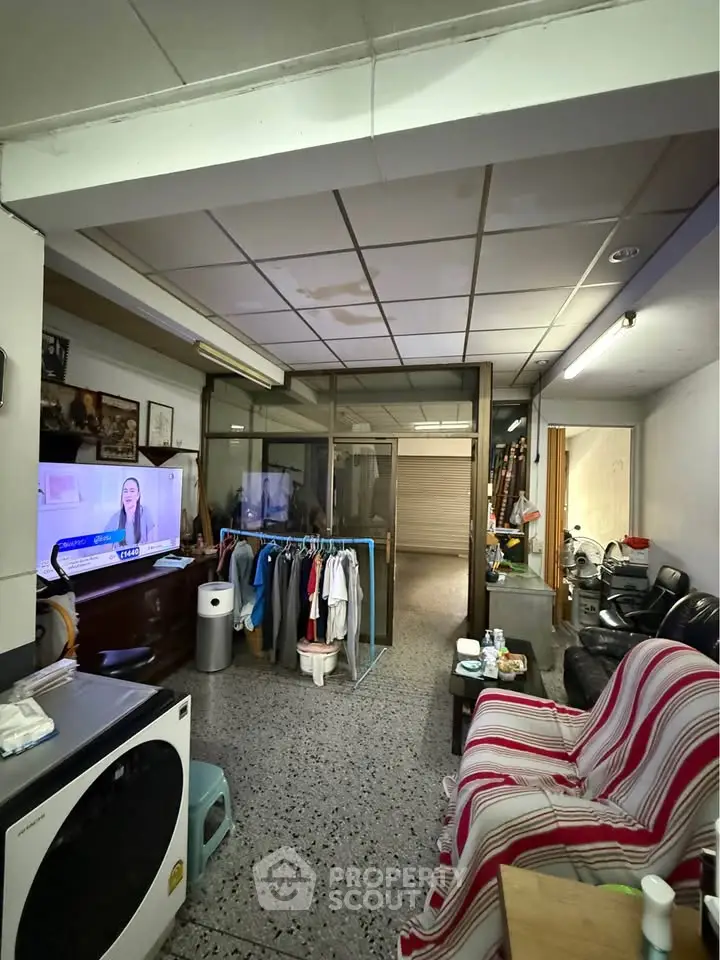 Cozy living room with TV and laundry area, featuring a comfortable sofa and tiled flooring.
