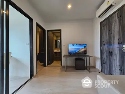 Modern minimalist living room with sleek furniture, wood-textured wall, and large sliding glass door leading to another room, creating a bright and airy space.