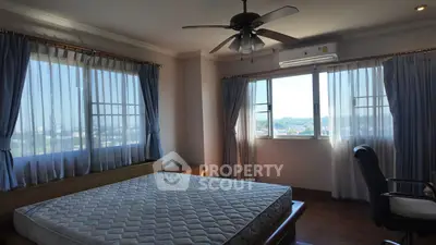 Spacious bedroom with large windows and ceiling fan, offering a serene view.