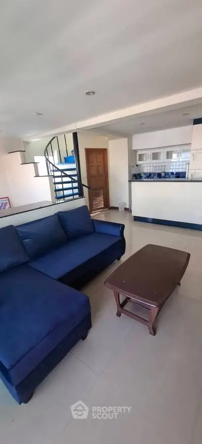 Spacious living room with modern blue sofa and open kitchen layout, featuring a stylish spiral staircase.