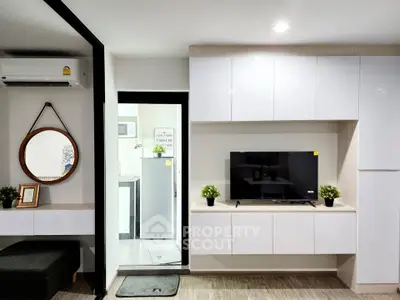 Modern living room with sleek white cabinetry and wall-mounted TV, adjacent to a compact kitchen area.