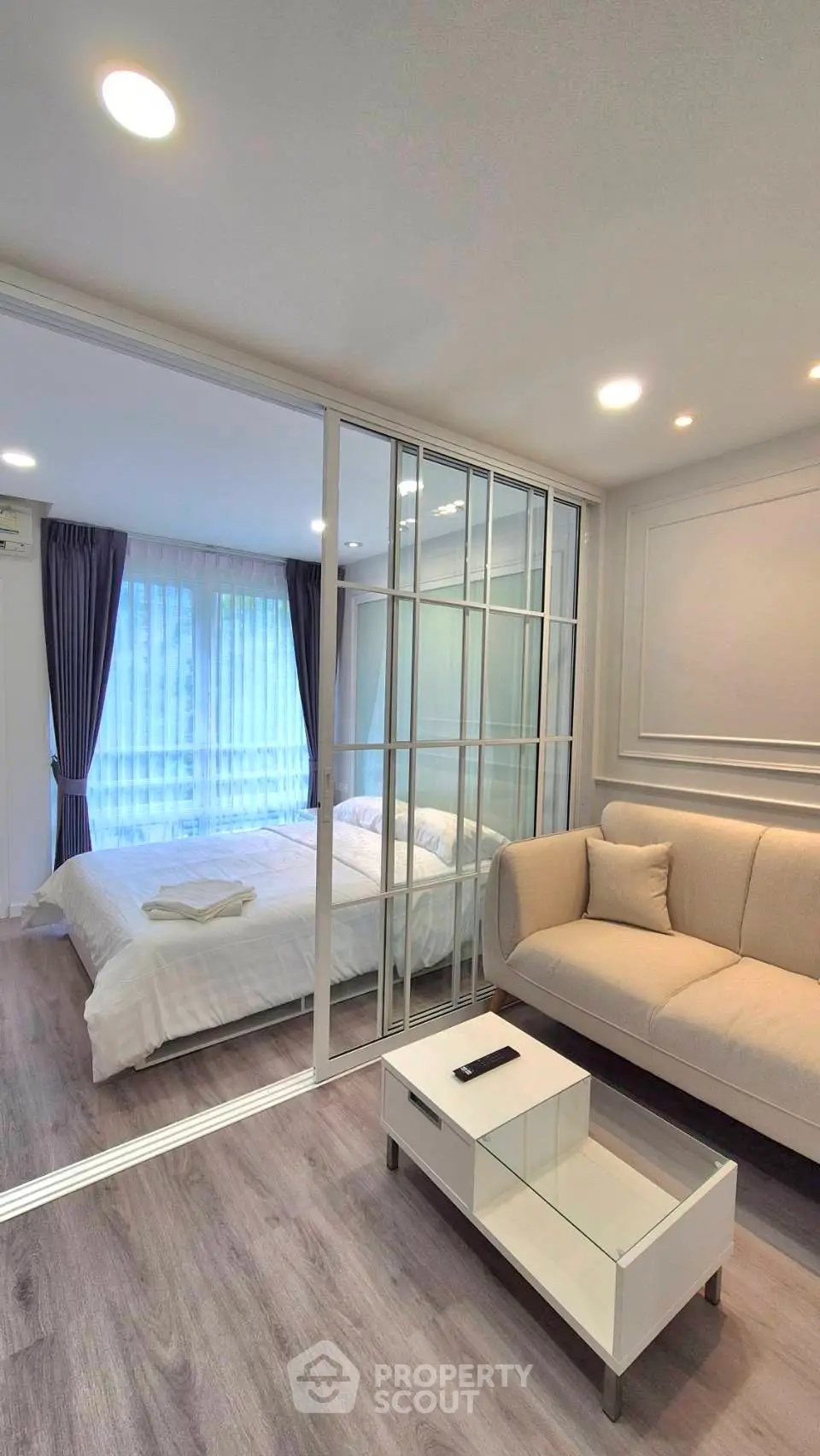 Modern living room with glass partition leading to cozy bedroom