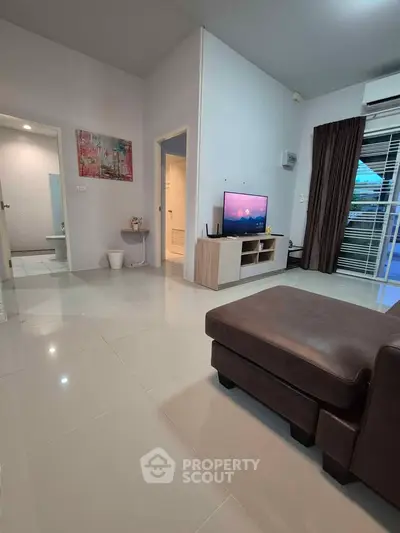 Modern living room with sleek furniture and TV, leading to a balcony with natural light.