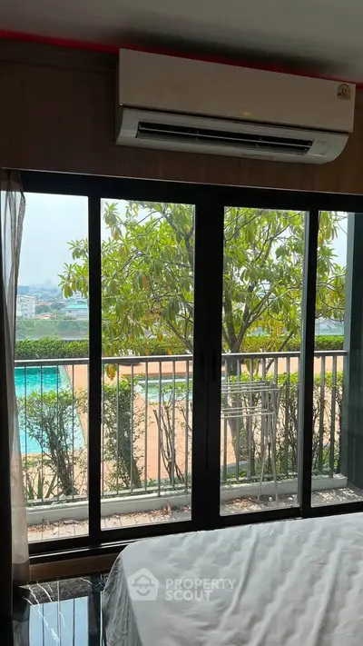 Spacious bedroom with large windows offering a stunning pool view and lush greenery, perfect for relaxation.