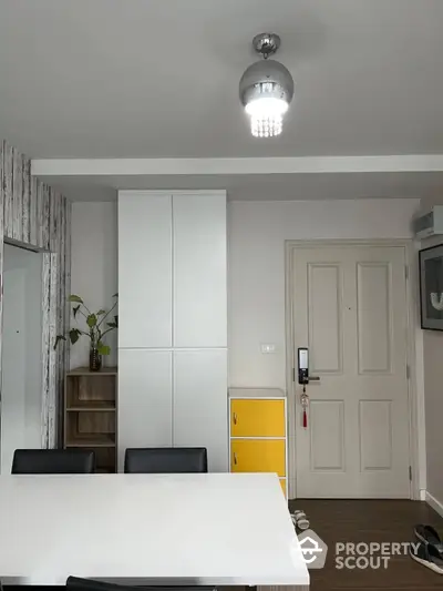 Modern minimalist living room with sleek white storage cabinets and a vibrant yellow fridge, complemented by warm wooden flooring and chic lighting.