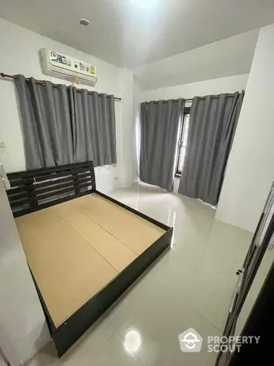 Spacious and well-lit bedroom with a large window, modern air conditioning unit, and elegant dark curtains complementing the minimalist decor.