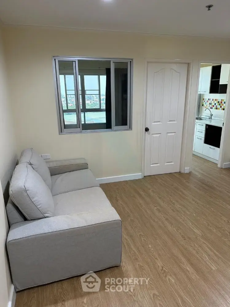 Spacious living room with modern sofa and view of kitchen, featuring wooden flooring and natural light.
