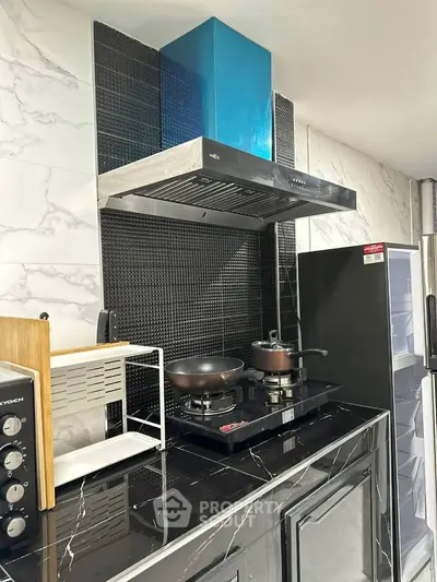 Modern kitchen with sleek black countertops and gas stove, featuring stylish backsplash and appliances.