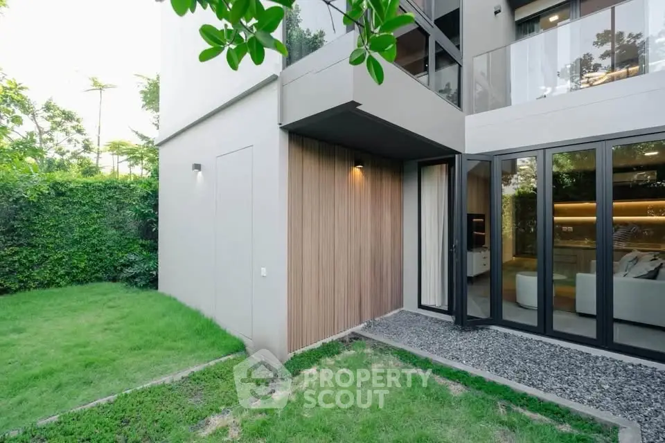 Modern home exterior with lush garden and large glass doors leading to a stylish living room.