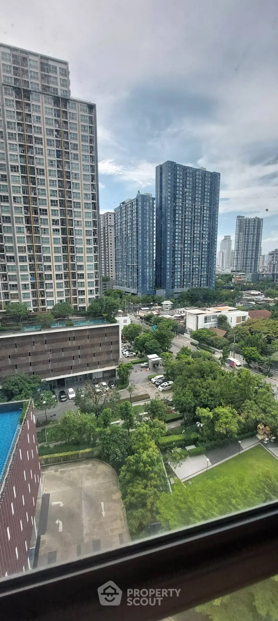 Stunning cityscape view from high-rise apartment window showcasing modern skyscrapers and lush greenery.