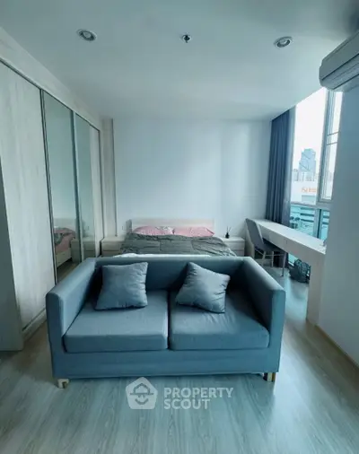 Modern studio apartment with cozy bed and stylish sofa, featuring large windows and city view.
