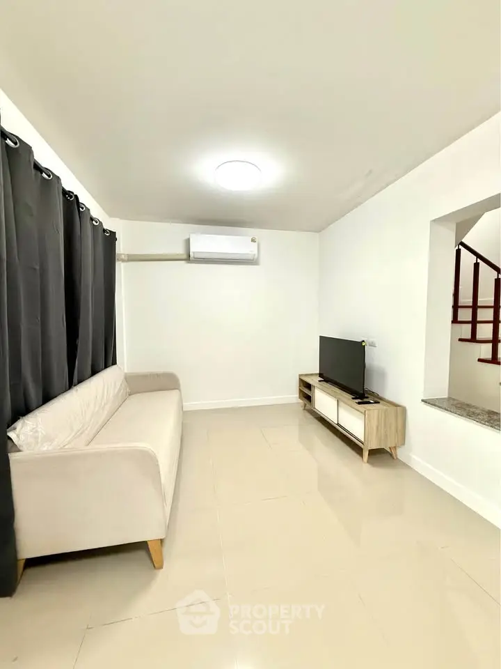 Modern living room with sleek sofa, TV unit, and air conditioning in a bright, minimalist space.