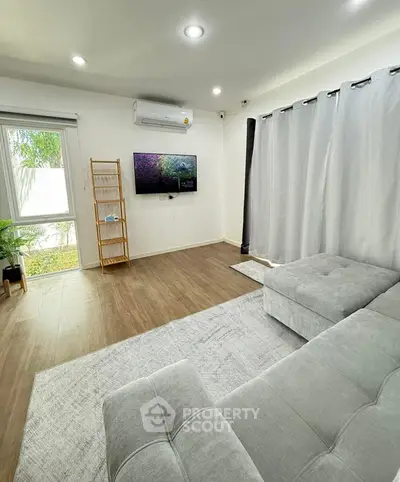 Modern living room with sleek design, featuring a cozy gray sofa, wall-mounted TV, and natural light from large window.