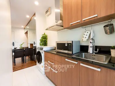 Modern kitchen with wooden cabinets, washing machine, and dining area in open layout apartment.