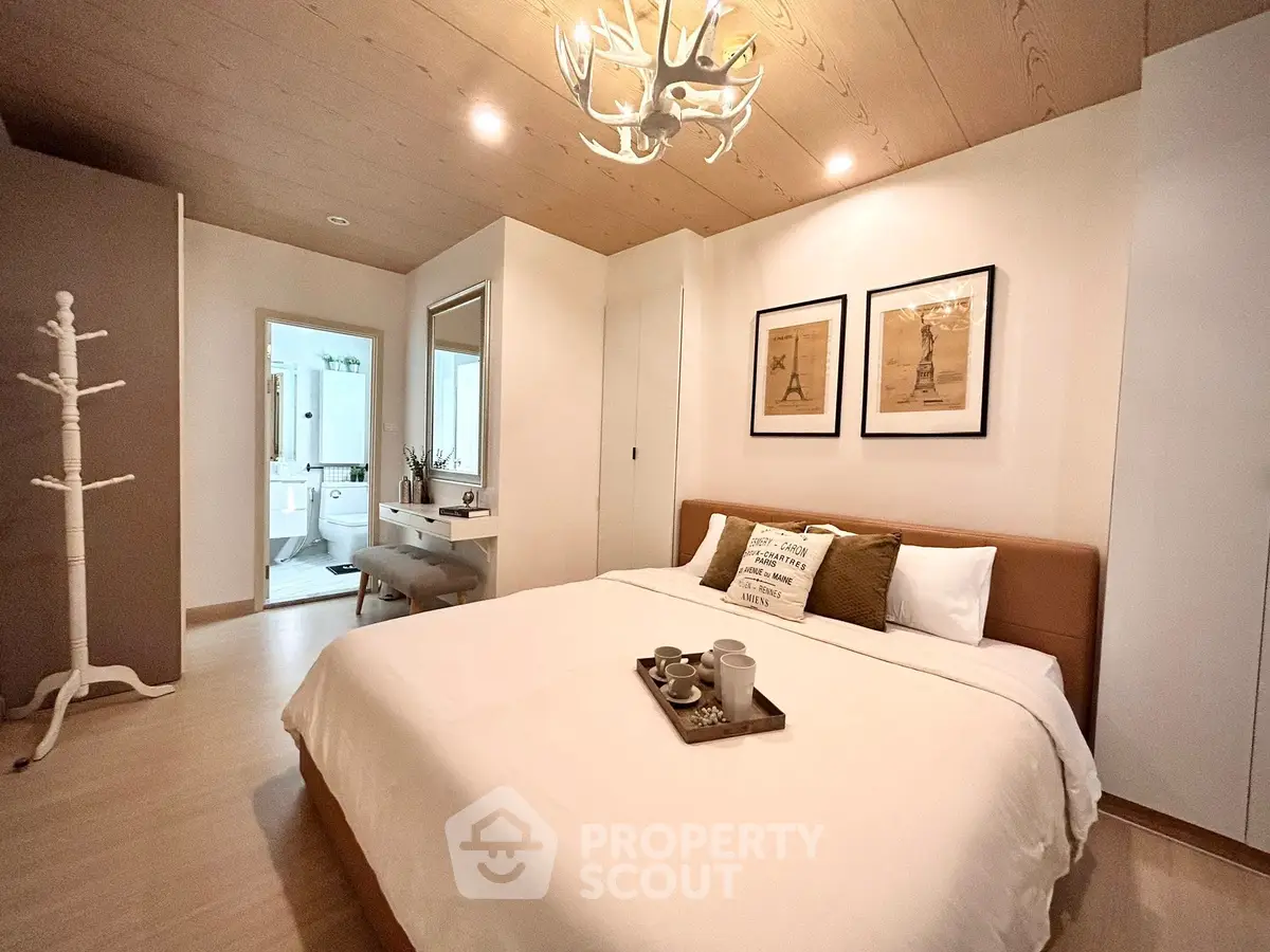 Cozy bedroom with modern decor and ensuite bathroom, featuring a stylish chandelier and wooden accents.
