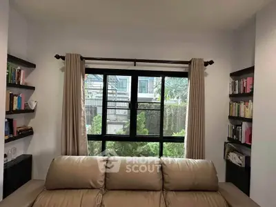 Cozy living room with a large window and bookshelves, perfect for relaxation and reading.
