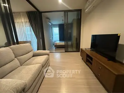 Modern living room with cozy sofa and TV unit, featuring sliding glass doors to bedroom.