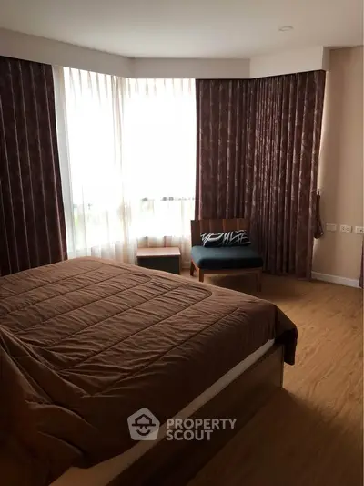Cozy bedroom with large window and elegant curtains, featuring a comfortable bed and stylish chair.