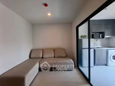 Modern living room with cozy sofa and adjacent kitchen featuring appliances.