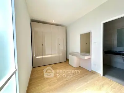 Spacious bedroom with modern wardrobe and vanity, featuring natural light and elegant wooden flooring.