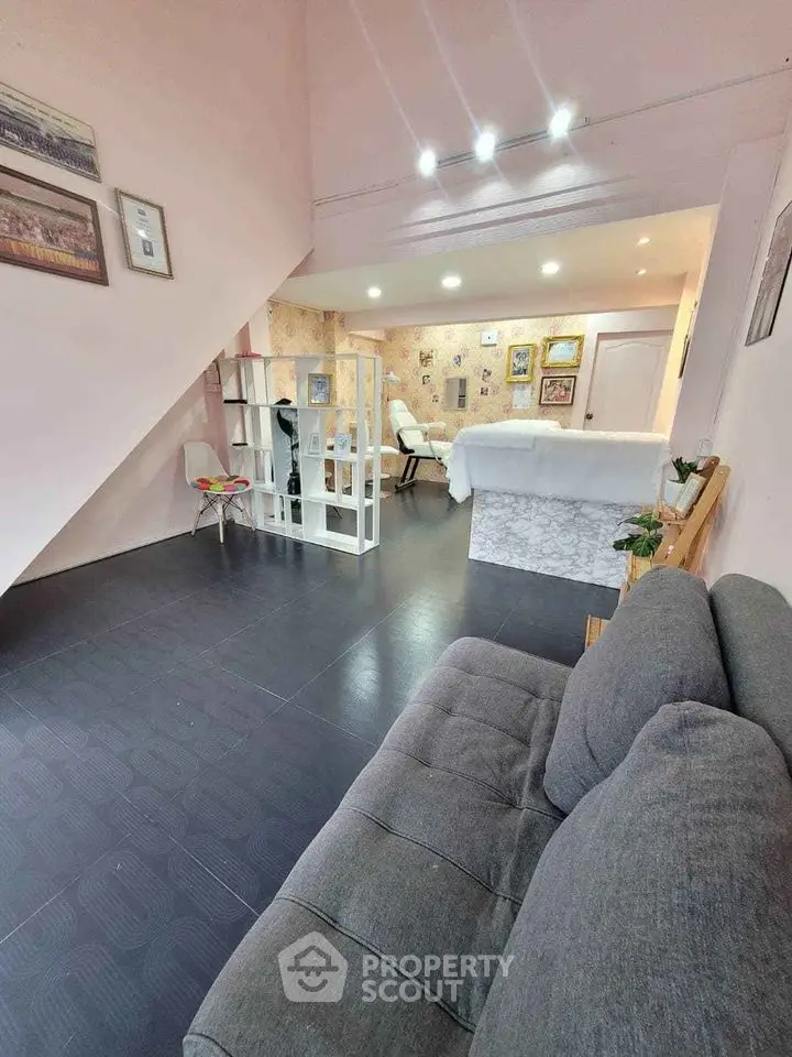Charming attic bedroom with cozy living space, featuring sleek dark flooring, comfortable grey sofa, and ambient lighting, ideal for a modern urban retreat.