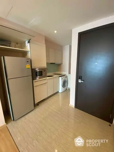 Compact modern kitchen with built-in appliances and ample storage, featuring a refrigerator, microwave, and washing machine, ideal for urban living.