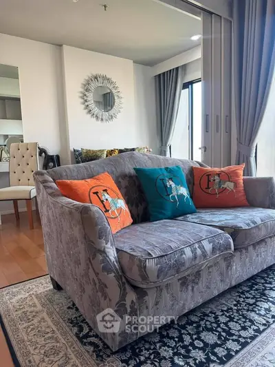 Elegant living room with stylish sofa and decorative pillows, featuring a sunburst mirror and floor-to-ceiling windows.