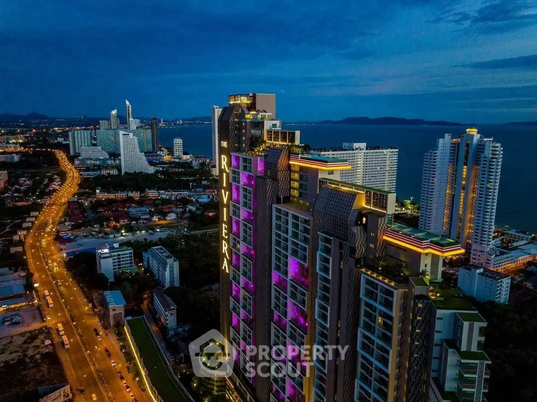 Stunning aerial view of luxury high-rise building with vibrant cityscape and ocean backdrop at dusk.