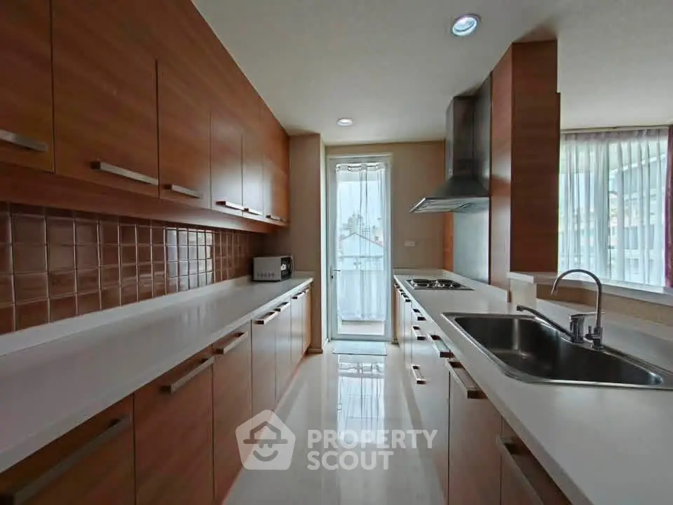 Spacious modern kitchen with sleek wooden cabinets and large windows for natural light.