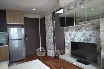 Modern living room with stylish wallpaper, sleek TV setup, and compact kitchen area.