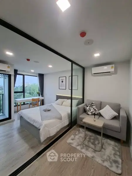Modern bedroom with glass partition and cozy seating area, featuring stylish decor.