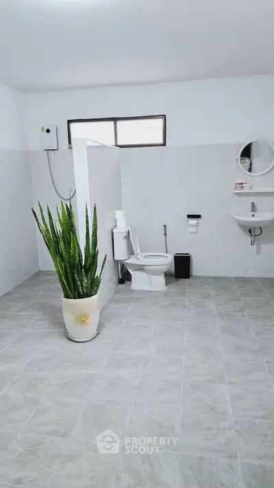 Spacious modern bathroom with sleek tiles and a large potted plant, featuring a minimalist design.
