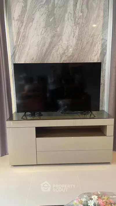 Modern living room with sleek TV stand and large flat-screen TV against a marble accent wall.