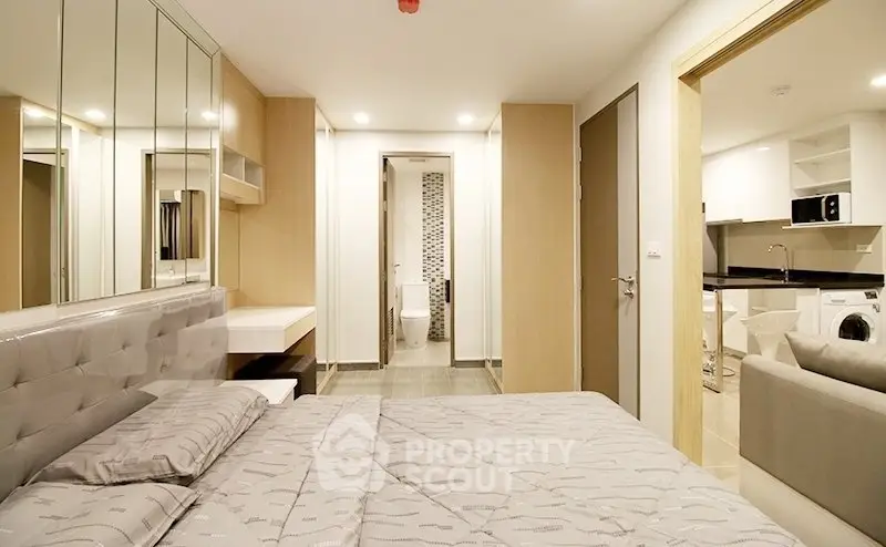 Modern bedroom with ensuite bathroom and open kitchen layout in stylish apartment.