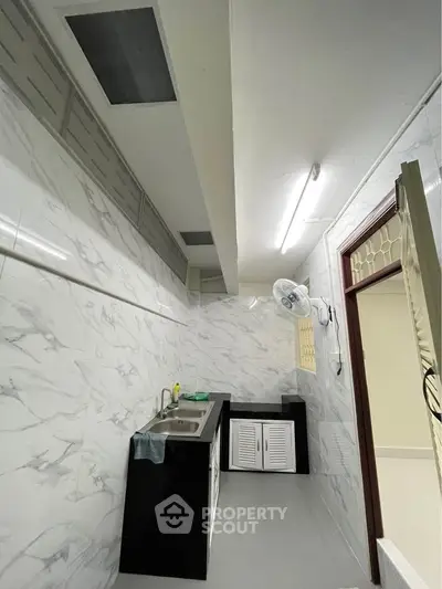 Modern kitchen with sleek black and white design, featuring marble walls and stainless steel sink.