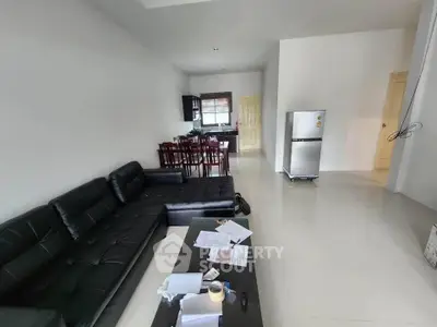 Spacious open-plan living room with modern black leather sofa and sleek kitchen area.