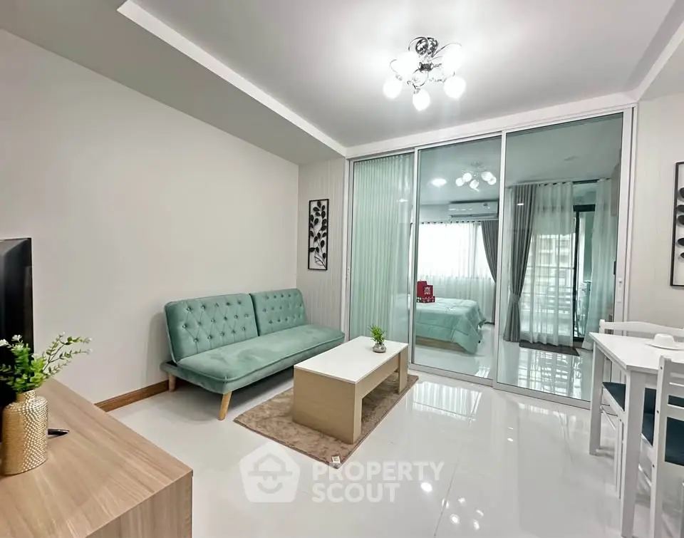 Modern living room with stylish furniture and glass partition leading to bedroom.