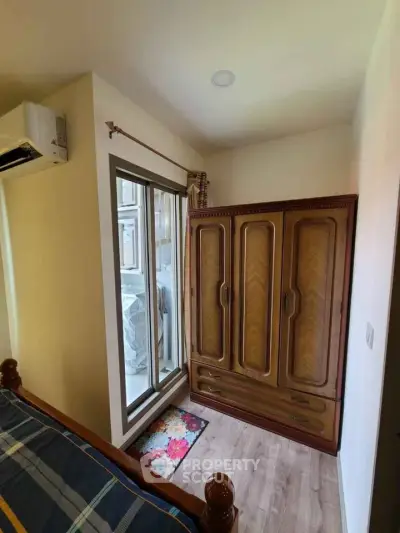 Cozy bedroom with wooden wardrobe and balcony access, featuring natural light and modern air conditioning.