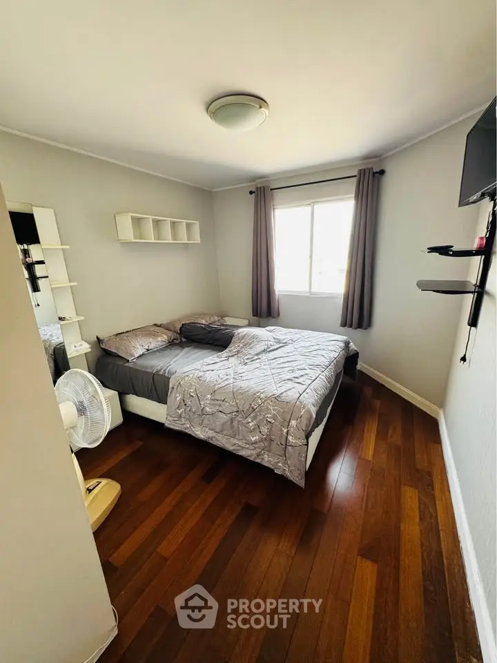 Cozy bedroom with wooden flooring and natural light, featuring a comfortable bed and modern decor.