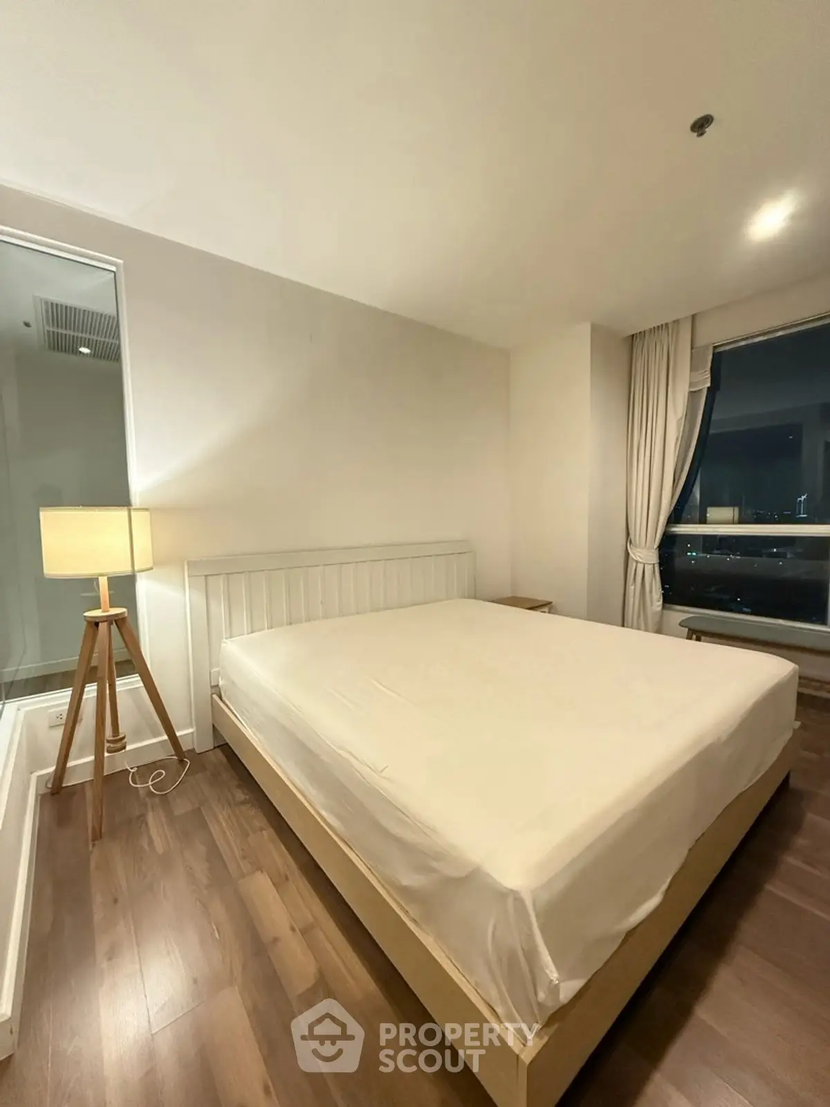 Modern bedroom with wooden flooring and large window offering city view.