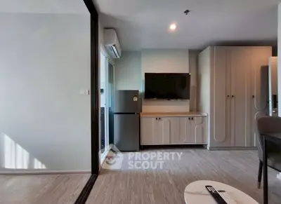 Modern living room with sleek furniture and large TV, featuring a compact fridge and ample storage space.