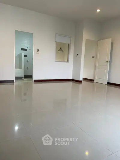 Spacious empty room with glossy tiled floor and open door to bathroom