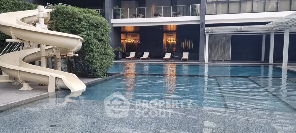 Luxurious pool area with slide and sun loungers in modern residential complex.