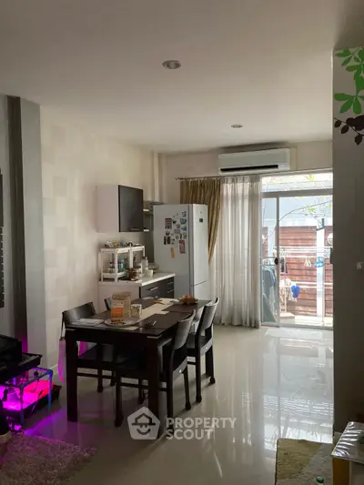Modern dining area with open kitchen and balcony access, featuring sleek furniture and natural light.