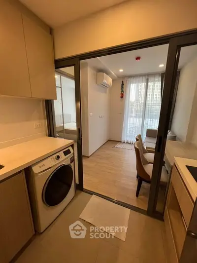 Modern apartment with compact kitchen and cozy living area, featuring a washing machine and sleek design.