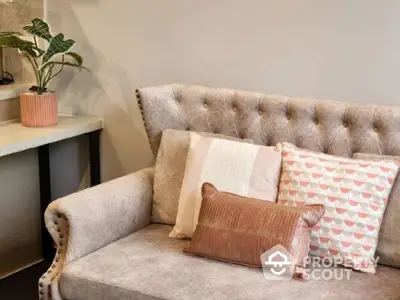 Elegant tufted sofa adorned with decorative pillows, complemented by a stylish plant and modern side table, perfect for a chic living space.