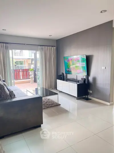 Modern living room with sleek furniture and large TV, featuring a bright balcony view.