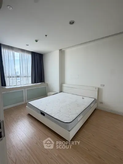 Spacious bedroom with large window and wooden flooring in modern apartment