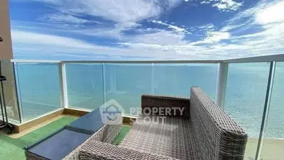 Stunning ocean view from a modern balcony with glass railing and wicker furniture.